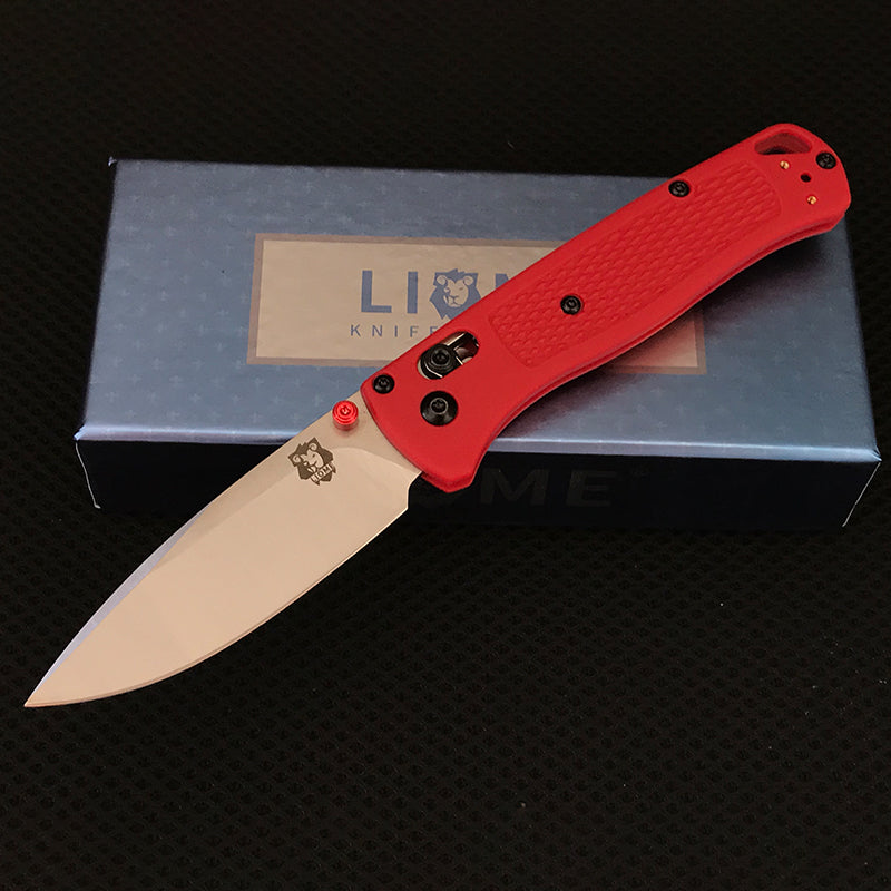 Red handled folding knife with polished silver drop-point blade and red pivot accent open on a Liome box