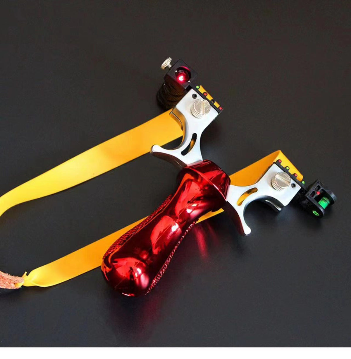 Red slingshot with yellow flat bands and a leather pouch laid on a dark table