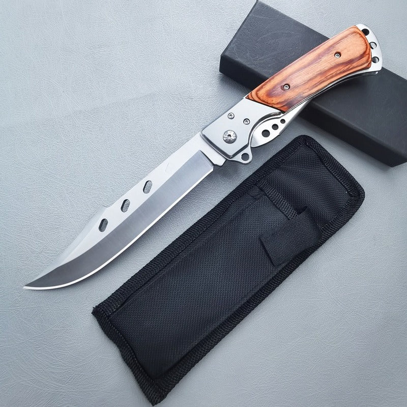Open redwood handle folding knife laid beside black nylon pouch on gray surface