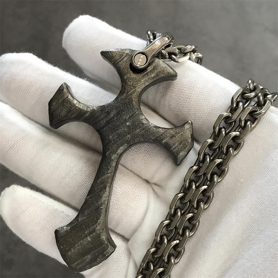 Relic finish TC21 titanium cross pendant held in a white gloved hand with stonewashed brushed texture