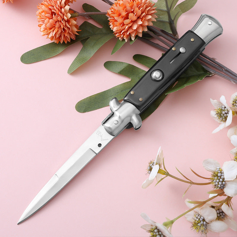 Black handle folding knife with polished blade on pink floral background