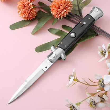 Black handle folding knife with polished blade on pink floral background