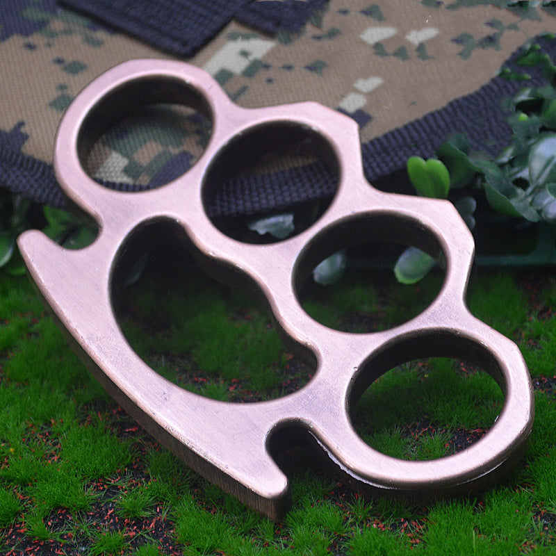 Rose Gold-J aluminum knuckle duster on camouflage fabric and grass, another side view