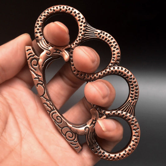 Rose gold Medusa pattern knuckle duster held in hand with serpent-scale finger rings and embossed face detail