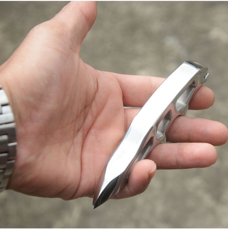 Side profile of the slim steel knuckle duster held low over an open palm showing the curved spine and tapered point