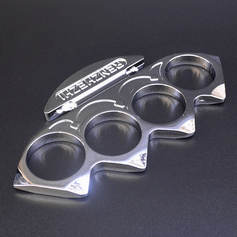 Silver knuckle duster lying flat on a dark surface with the embossed palm plate at the back