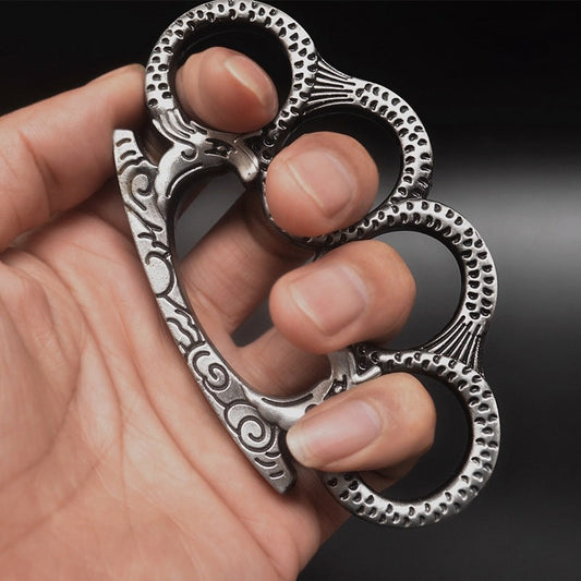 Silver Medusa pattern knuckle duster gripped in hand showing four finger holes and textured palm bar