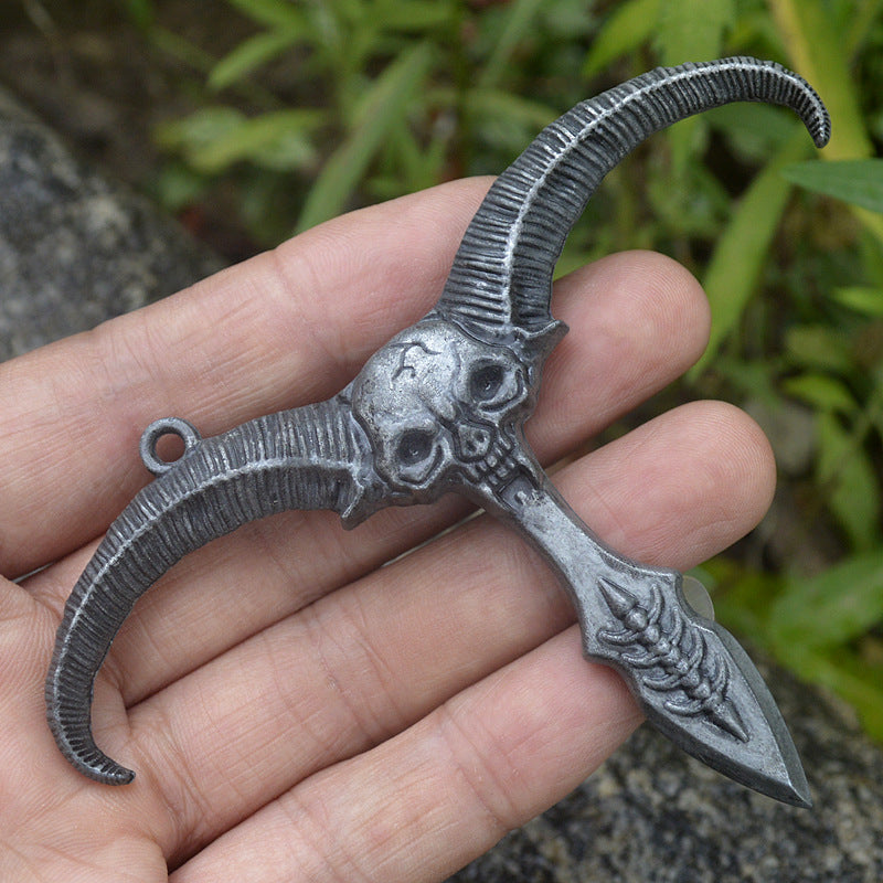 Silver gray sheep skull pendant held across an open palm showing the ribbed horns and dagger style point outdoors