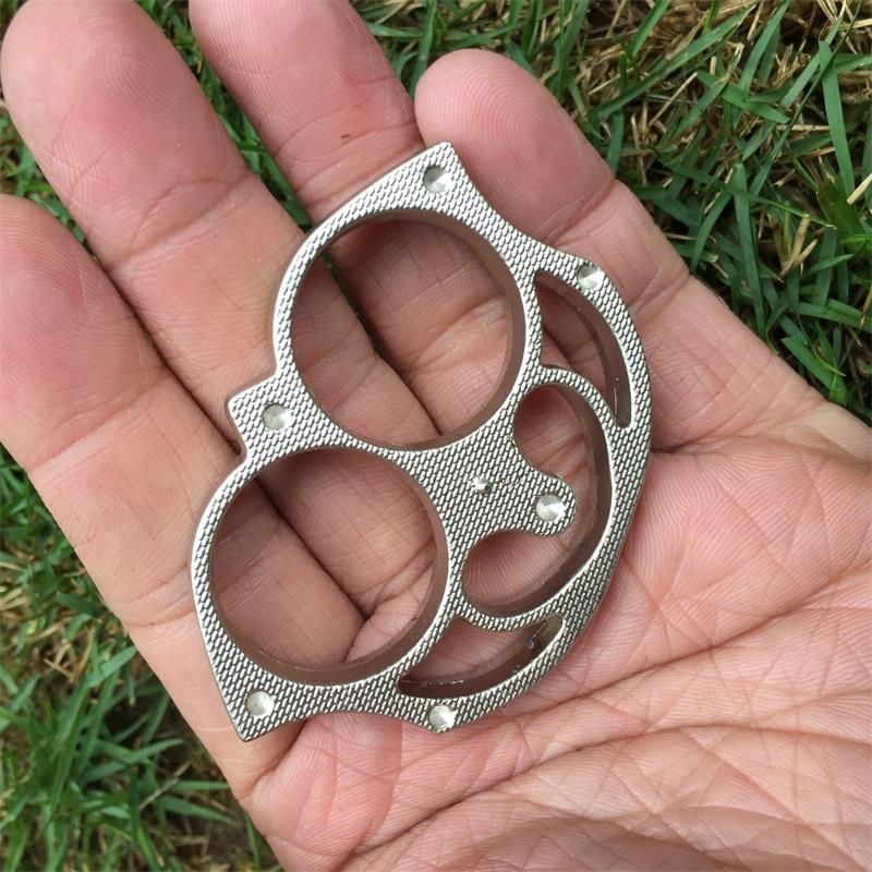 Silver sloth finger clasp lying in an open palm over grass showing the sloth face outline and rivet studs