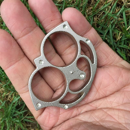Silver sloth finger clasp lying in an open palm over grass showing the sloth face outline and rivet studs