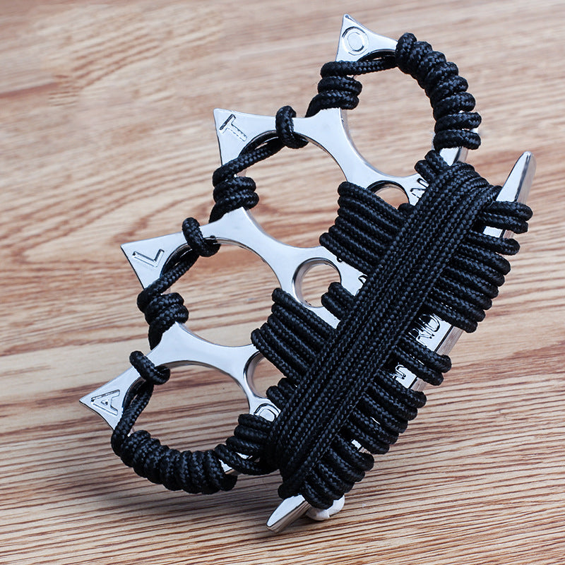 Silver four-finger knuckle duster with black umbrella cord wraps across the palm plate, set on a light wooden table