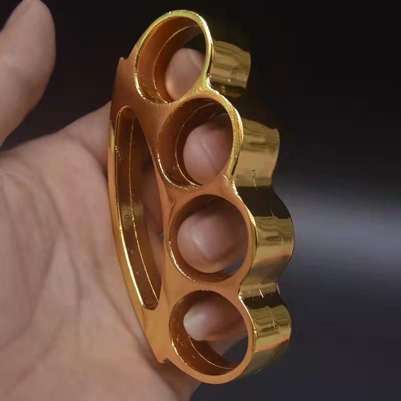 Gold smile-hole zinc alloy knuckle duster held in hand showing side profile and finger holes