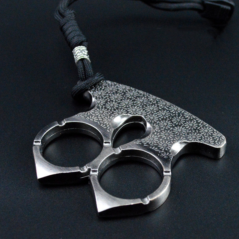Steel gray two-finger knuckle with floral engraving lying flat on a dark surface, cord through the top