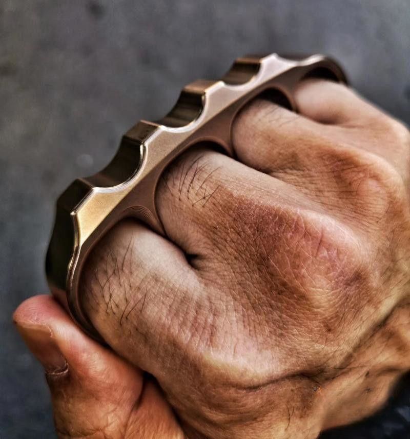 Close view of a fist wearing the bronze toned steel knuckle with the wavy top rail across the knuckles