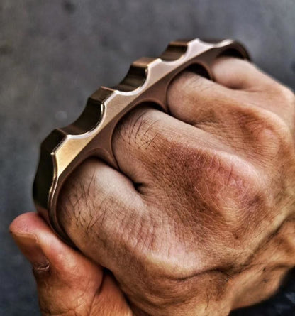 Close view of a fist wearing the bronze toned steel knuckle with the wavy top rail across the knuckles