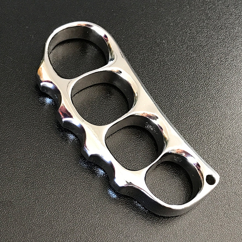 Bright polished steel knuckle lying flat on a dark textured surface with its lanyard hole at the end