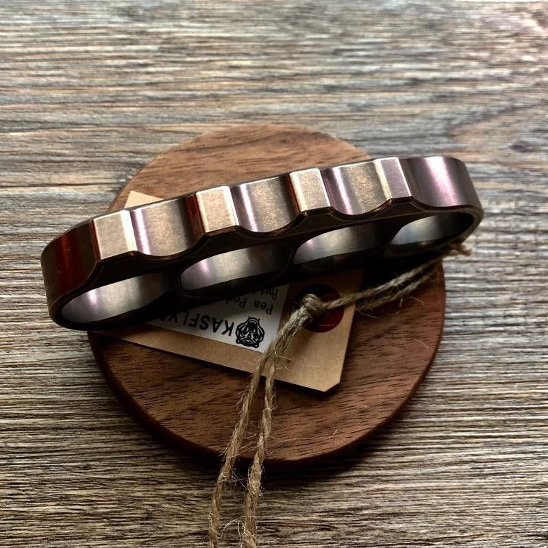 Bronze toned steel knuckle standing upright on a wooden coaster showing the scalloped top rail
