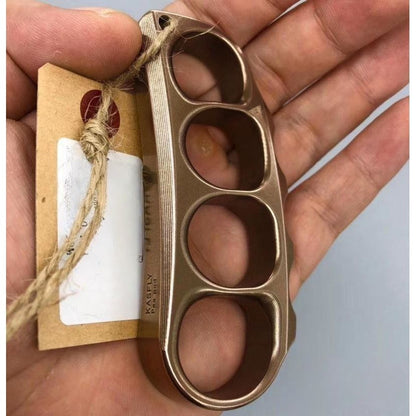 Hand holding the bronze toned steel knuckle with a kraft paper tag tied through the lanyard hole