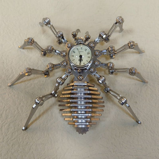 Mechanical spider sculpture with cream clock face and stacked steel abdomen viewed from above on a light leather surface