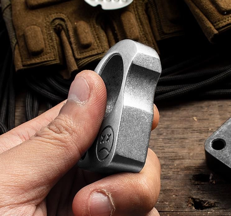 Metal storage tin set with a silver-tone knuckle weight and camo cord in black foam, the engraved lid resting beside it