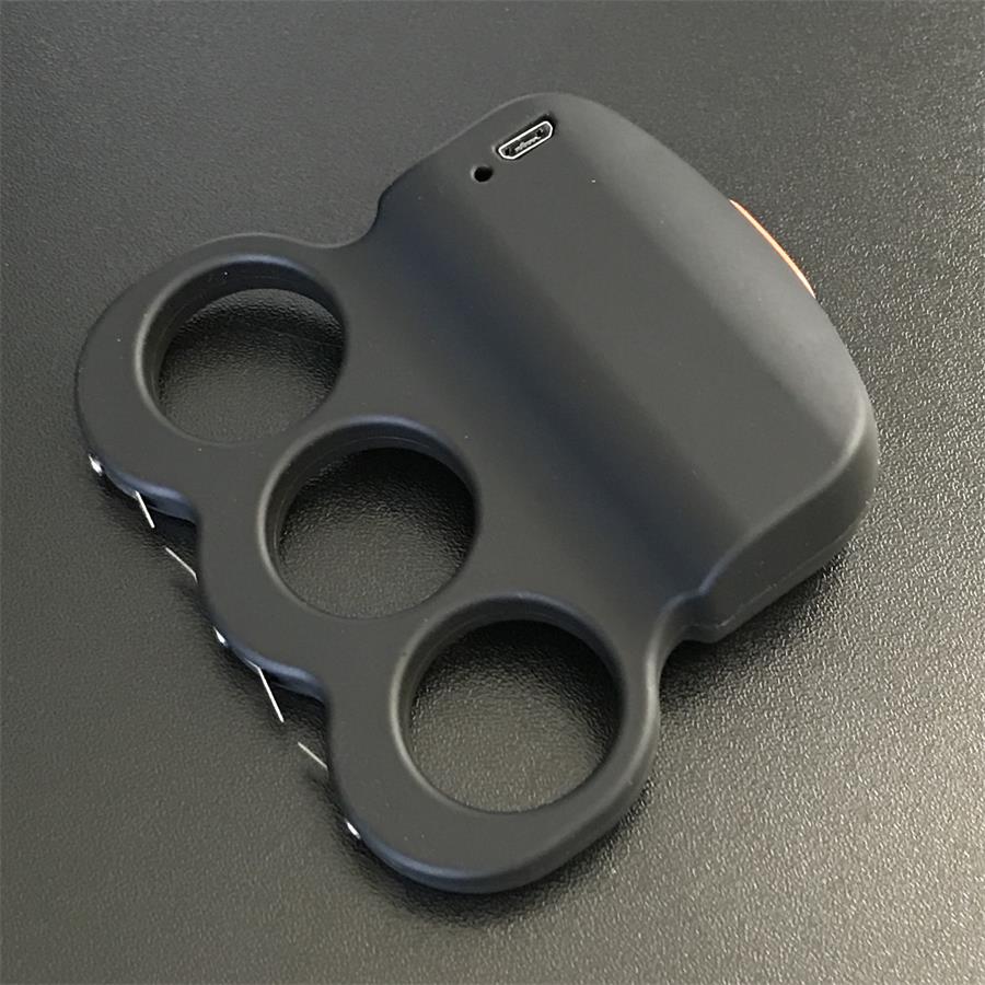 Black three-hole stun device on a dark surface with the USB charging port on the top plate, orange button on the right edge and prong points at the lower left