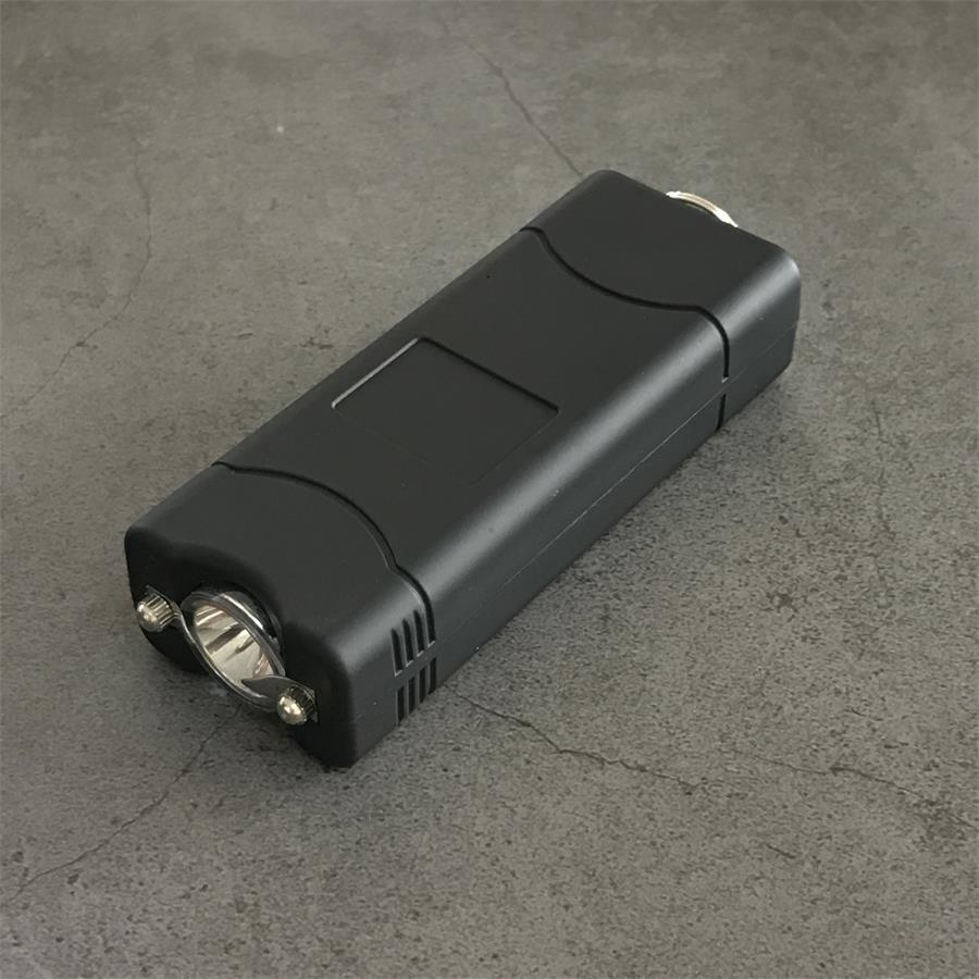 Black 801C stun gun held in a white-gloved hand with the light switched on and red indicator lit