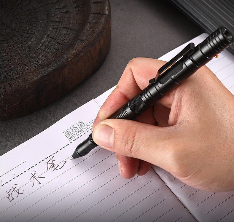 A hand writes with the black tactical pen on lined notebook paper, leaving handwritten characters beside printed grid boxes, with a wooden stump in the background.