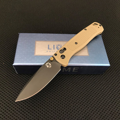 Desert tan handled folding knife with black-coated blade and brass pivot accent open on a Liome box