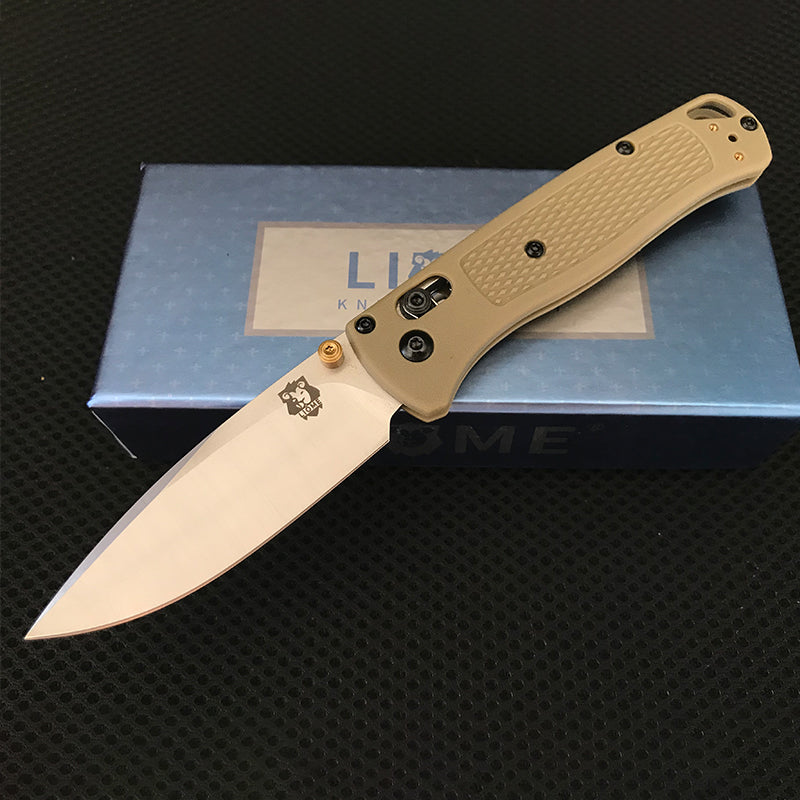 Desert tan handled folding knife with polished silver blade and brass pivot hardware open on a Liome box