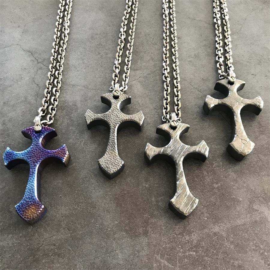 Four TC21 titanium cross necklaces in Blaze, Titan, Relic and Obsidian finishes laid on dark stone