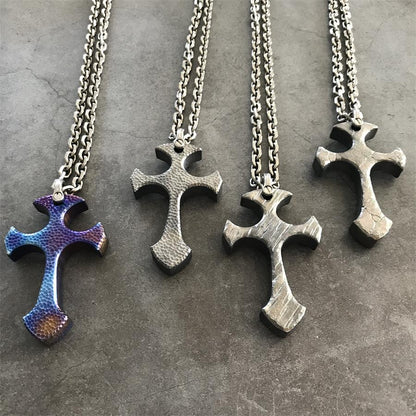 Four TC21 titanium cross necklaces in Blaze, Titan, Relic and Obsidian finishes laid on dark stone
