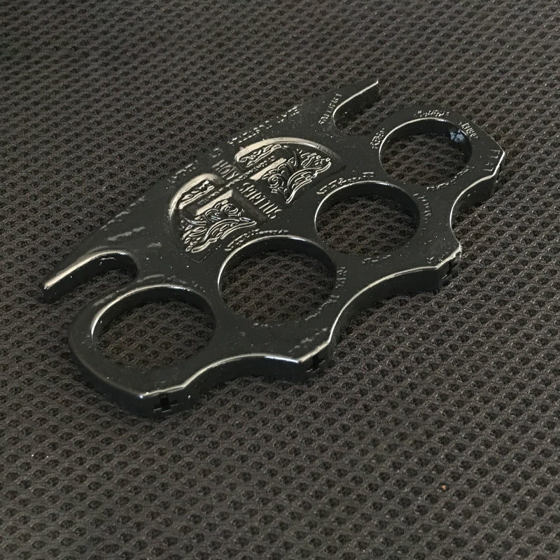 Black knuckle duster lying on a dark textured mat with the shield emblem catching the light