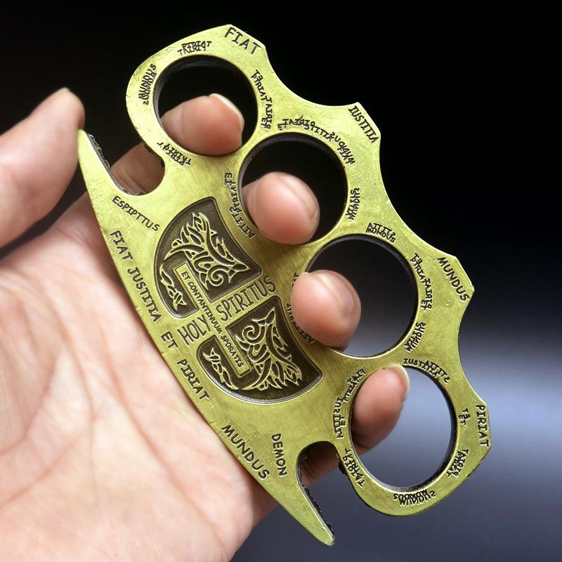 Golden knuckle duster held face up showing the engraved shield crest and lettering around the frame