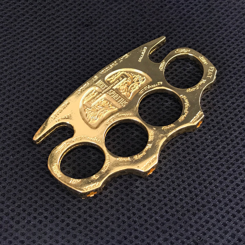 Golden knuckle duster viewed from above on a black textured mat showing the full engraved design