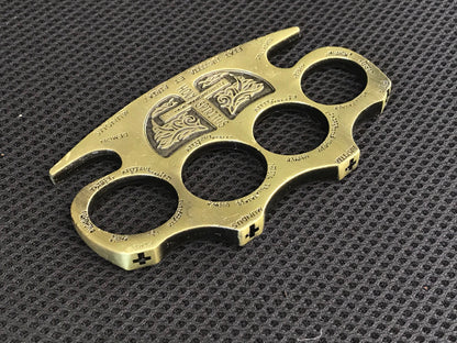 Wide view of the golden knuckle duster on a textured mat showing the engraved shield and side cross marks