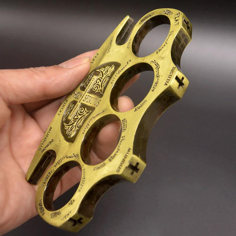 Hand holding the golden knuckle duster at an angle showing the cross markings along the side edges