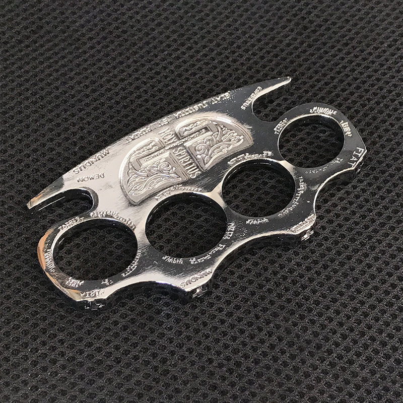 Silver knuckle duster lying on a black textured mat showing the engraved face and pointed lower tip