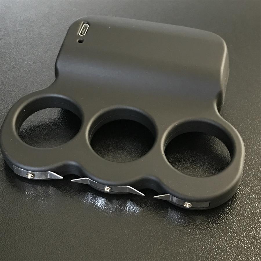 Black three-hole stun device lying flat showing the three finger rings, USB charging port on the top edge and prong points along the lower left edge
