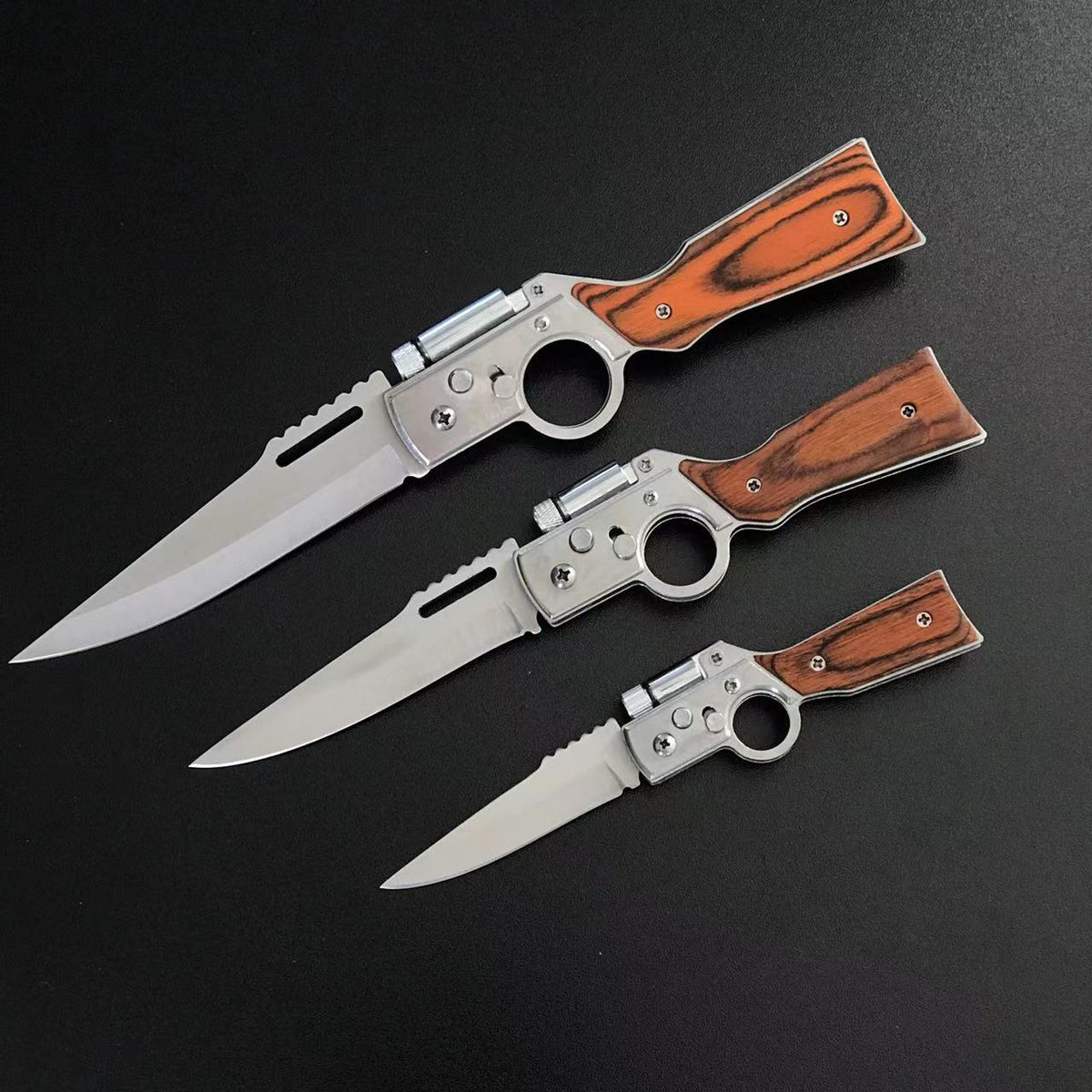 Three wood-handle folding pocket knives in Large, Medium and Small sizes open on black tactical fabric