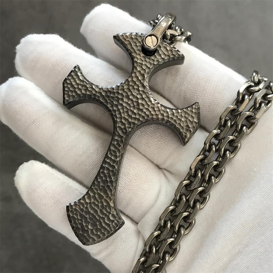 Titan finish TC21 titanium cross pendant in a white gloved hand with raw gray hammered texture