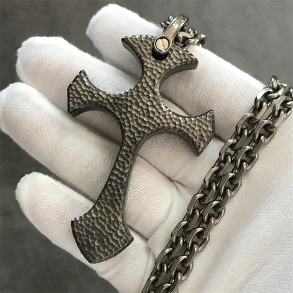 Titan finish TC21 titanium cross pendant in a white gloved hand with raw gray hammered texture