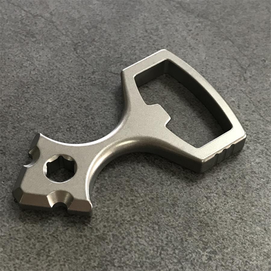 Angled view of the titanium opener tool showing the hex socket head and the finger loop with ribbed corner