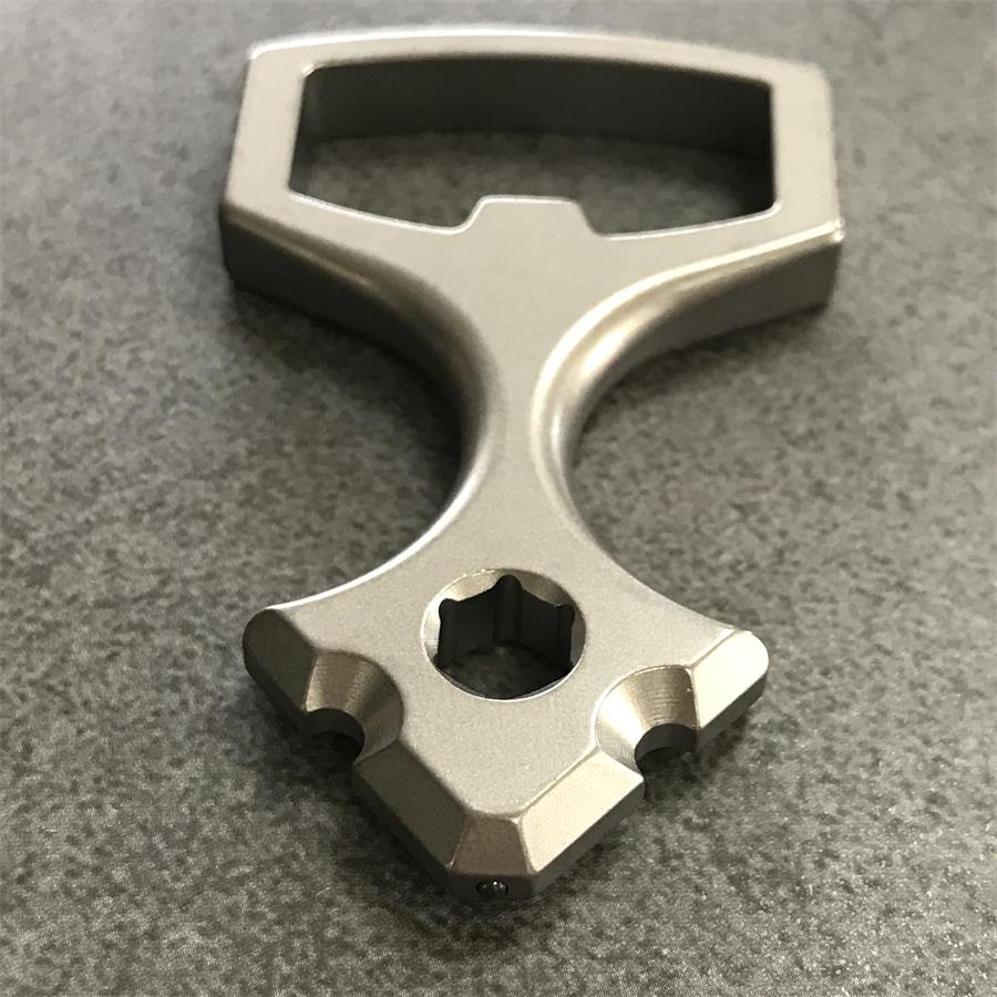 Close three-quarter view of the titanium opener tool showing the stepped lip inside the finger loop