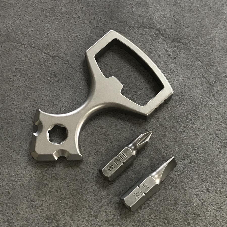 Titanium opener tool beside two screwdriver bits marked S2 on a grey textured surface