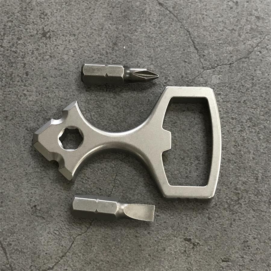 Titanium bottle opener tool laid out with a Phillips bit and a slotted bit on a grey stone surface