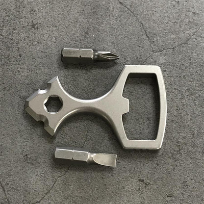 Titanium bottle opener tool laid out with a Phillips bit and a slotted bit on a grey stone surface