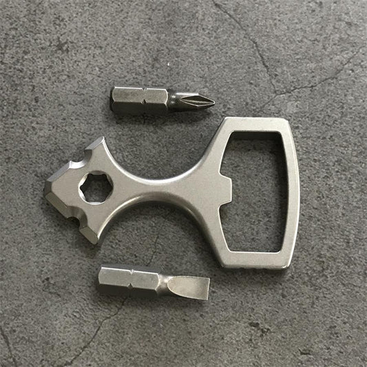 Titanium bottle opener tool laid out with a Phillips bit and a slotted bit on a grey stone surface