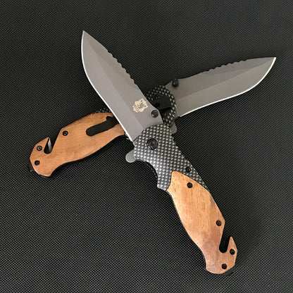Two Liome X50 folding knives crossed on a dark mat showing wood scales, carbon fiber pattern bodies and grey sawback blades