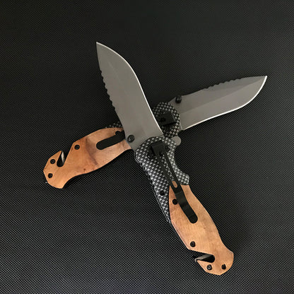 Two Liome X50 knives crossed in an X shape showing the wooden front handle and the carbon fiber back with clip