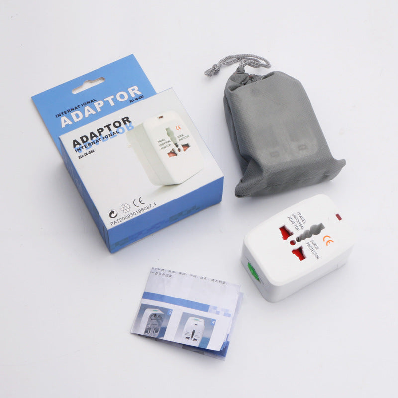 White universal travel adapter angled on soft white fabric showing the universal socket, the red indicator dot and the green lock slider
